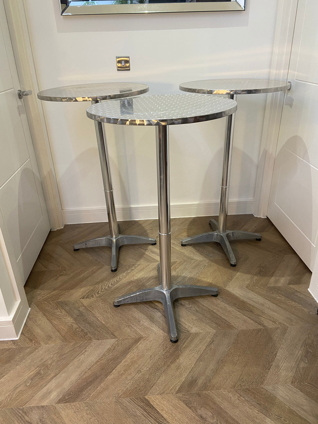 Three metallic side tables with glass tops on a wooden floor.