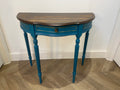 Blue half-moon table with a wooden top on a wooden floor.